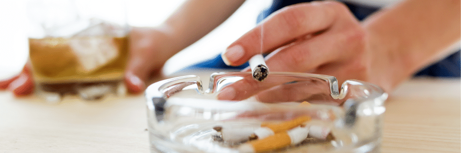 hands of a person smoking and the other is holding a glass of whisky